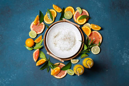 Citrus slices - orange,lemon and grapefruit with green leaves and citrus juice around empty plate on blue background, frame, top viewの写真素材