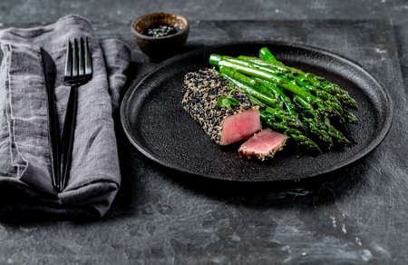 Fried tuna steak in black sesame with asparagus on black plateの写真素材