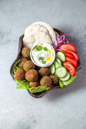 Falafel, fresh vegetables and pita bread on clay plate, gray background