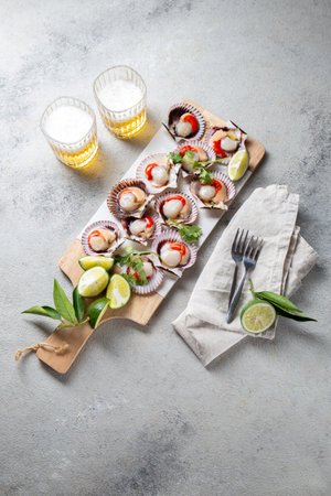 Raw Seafood shellfish scallops with lemon, cilantro and michelada beer drink on white board, gray backgroundの写真素材