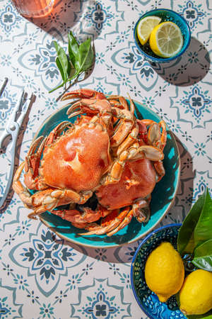 Cooked crab on blue plate, lemons, rose wine on table, sunlight immitationの写真素材
