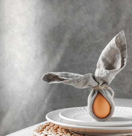Festive Easter table setting. Funny Easter bunny made of egg and linen napkin on plate. Gray background.の写真素材