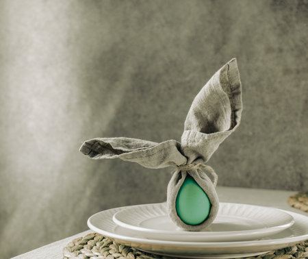 Festive Easter table setting. Funny Easter bunny made of green egg and linen napkin on plate. Gray background.の写真素材
