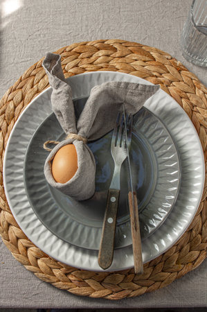 Festive Easter table setting. Funny Easter bunny made of egg and linen napkin on plate. Gray background.の写真素材