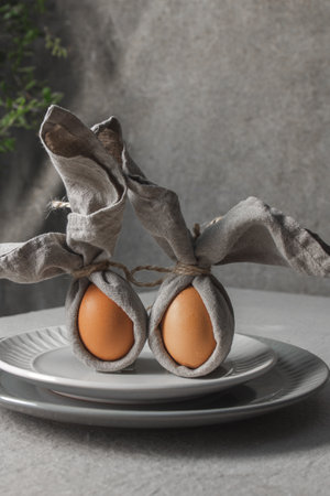 Festive Easter table setting. Funny Easter bunny made of egg and linen napkin on plate. Gray backgroundの写真素材