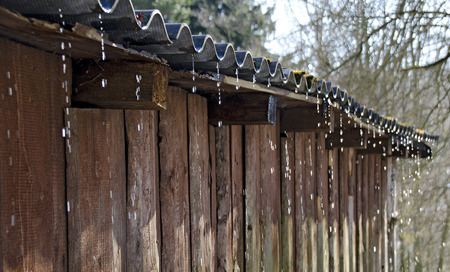 water diping from a wooden hut with corrugated eternit panelsの写真素材