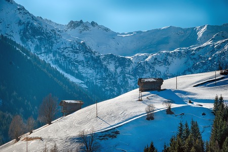snow covered winter scenery in the mountains with wooden hay huts at Gailvalley, Carinthia, Austria