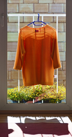 orange pullover in the sunshine at a railing of a balcony window