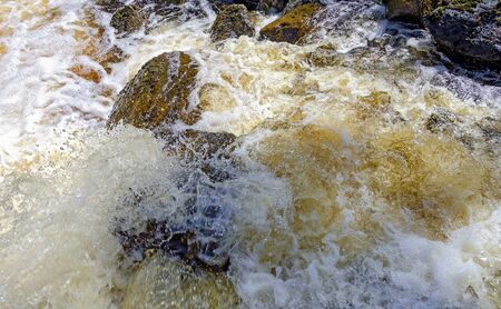 foaming and splashing gold coloured white water overflowing rocks in Sweden