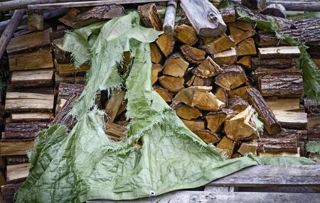 stack of logs of firewood partly covered by a torn sheet