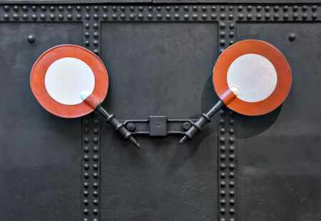 two signalling discs of the former Imperial-Royal State Railways of Austria on a black metal sheet with rivets showing the end of a trainの写真素材