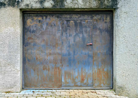old rusty garage gate with integrated door with handle in an old wallの写真素材