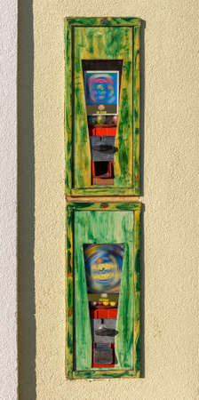 two gumball machines in old metallic boxes built into a wall