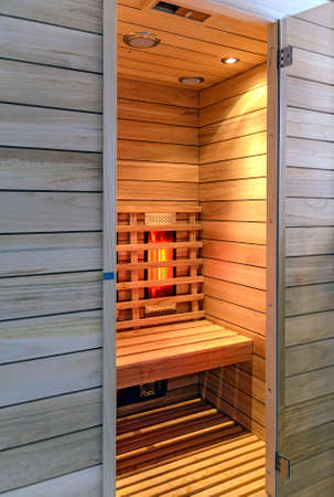 View into a wooden infrared cabin with glowing heating elements and open doorの写真素材