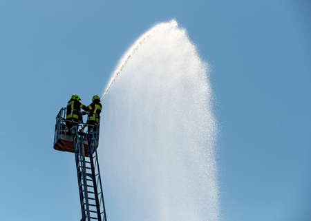 two fire fighters on a turntable ladder spraying water against the blue sky, Austriaの写真素材