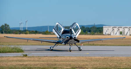 single engine silvery private plane with hinged up gull-wing doors at setdown position on an airport