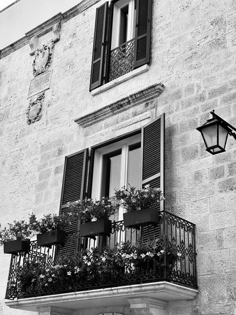 Black and white photo Charming Puglia architecture with window, flowers, shutters, and wrought iron balcony â scenic Southern Italy facade showcasing Mediterranean style and heritaの写真素材