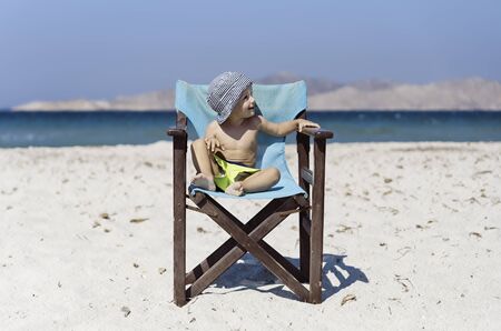 Little boy sitting in chair on beachの写真素材