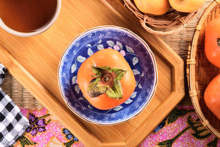 Delicious ripe persimmon fruit on wooden tray.