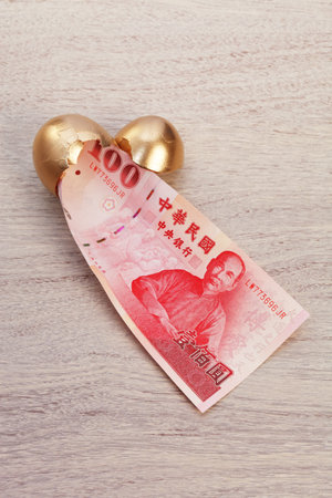 New Taiwan dollars in golden broken egg on wooden background.の写真素材