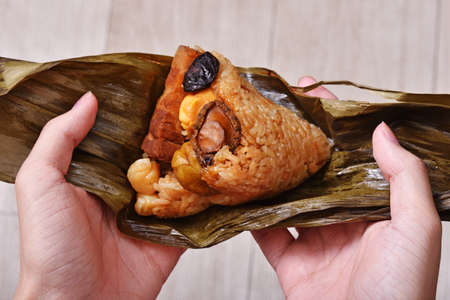 Hand holding zongzi (rice dumpling) with savoury fillings wrapped in bamboo or reed leaves.