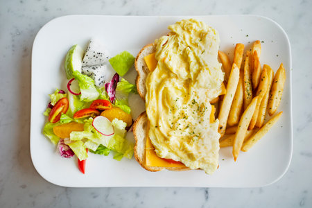Cheese scram bled egg, white bread loaf, mixed greens and french fries on the plateの写真素材