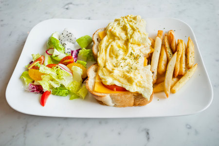 Cheese scram bled egg, white bread loaf, mixed greens and french fries on the plateの写真素材