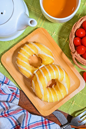 Donuts on a wooden plate with a cup of tea and tomatoesの写真素材