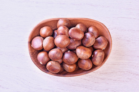 Top view of chestnuts in wooden bowl on white wooden background.の写真素材