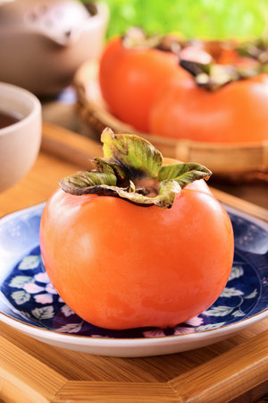 Persimmon on a plate with tea in the background, close upの写真素材