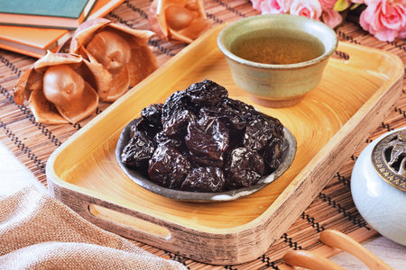 Dried black dates on black plate and tea on a wooden tray
