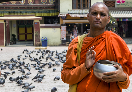Unidentified monk with bowl standing for alms and chanting at the famous attraction Buddhist Shrine Boudhanath Stupa, Kathmandu, Nepal.のeditorial素材