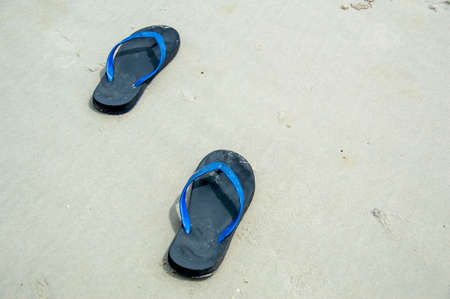 A pair of sandals on the sand during the day.
