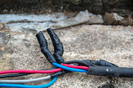 Electrical wires wrapped with black tape on a cement floor.