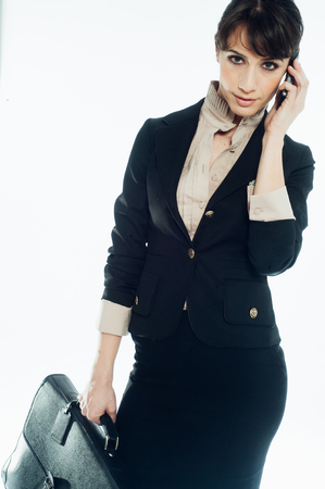 Young caucasian brunette suit dressed business woman talking with a vintage smartphone. Standing up. Studio shot.の写真素材