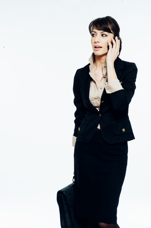 Young caucasian brunette suit dressed business woman talking with a vintage smartphone. Standing up. Studio shot.の写真素材