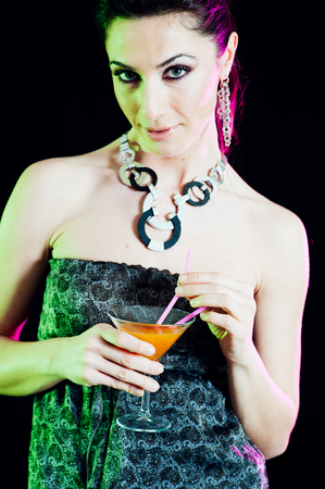 Young caucasian brunette taking aperitif with black background. Studio shotの写真素材