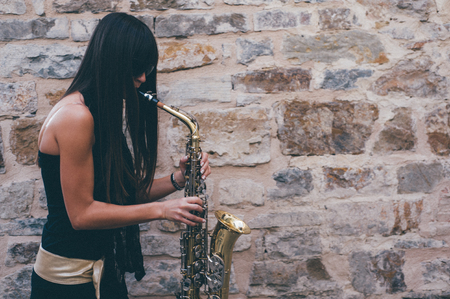 Young brunette girl having fun playing sax outdoor in a urban sceneの写真素材
