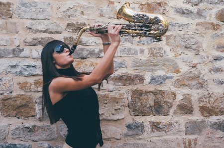 Young brunette girl having fun playing sax outdoor in a urban sceneの写真素材