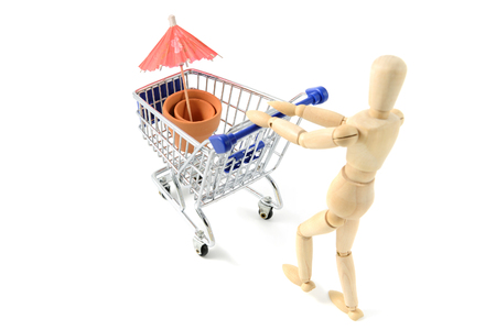 wooden mannequin shopping garden utensils in a shopping cart at white isolated background.の写真素材
