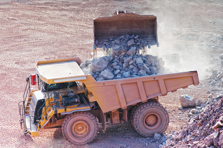 view into a quarry mine of porphyry rock. bulldozer loading dumper truck with rocks.