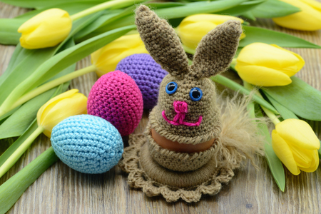 Crochet Easter bunny egg cup and easter eggs made of wool. background bunch of yellow tulipsの写真素材