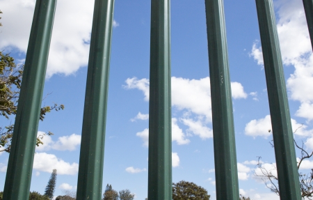 Exterme closeup of green spiked palisade fence against blue sky clouds and trees