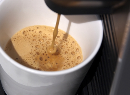 A closeup of a home espresso machine pouring a shot of espresso coffee into a white coffee cupの写真素材