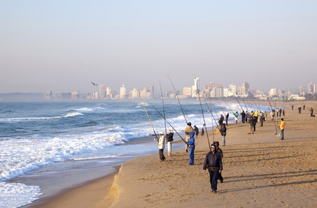 DURBAN, SOUTH AFRICA - JULY 2, 2014: Many unknown people fish on beach with city skyline in background in Durban, South Africaのeditorial素材