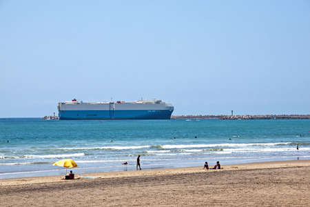 DURBAN, SOUTH AFRICA - SEPTEMBER 21, 2014: Many unknown people enjoy the morning on beach as large ship enters harbor in Durban, South Africaのeditorial素材