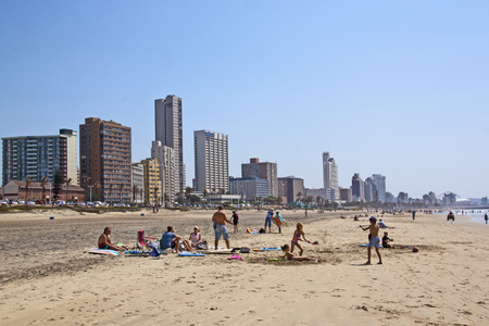 DURBAN, SOUTH AFRICA - SEPTEMBER 21, 2014: Many unknown people enjoy early morning sunshine at beach against city sky line in Durban, South Africaのeditorial素材