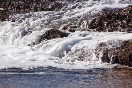 white foaming water streaming over seaweed covered rocksの写真素材