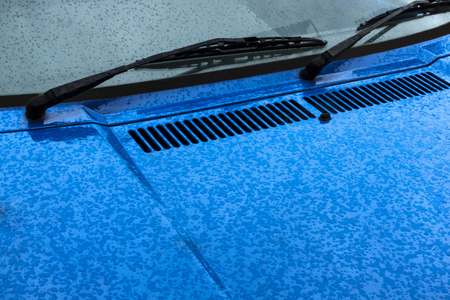 Close up of wiper arm and blade blue bonnet with water droplets and air vent on motor vehicleの写真素材