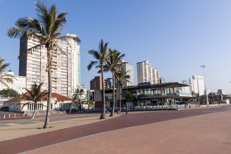 DURBAN, SOUTH AFRICA - JUNE 24, 2016: Early morning empty beach front paved promenade and palm trees  against Golden Mile city skyline in Durban, South Africaのeditorial素材